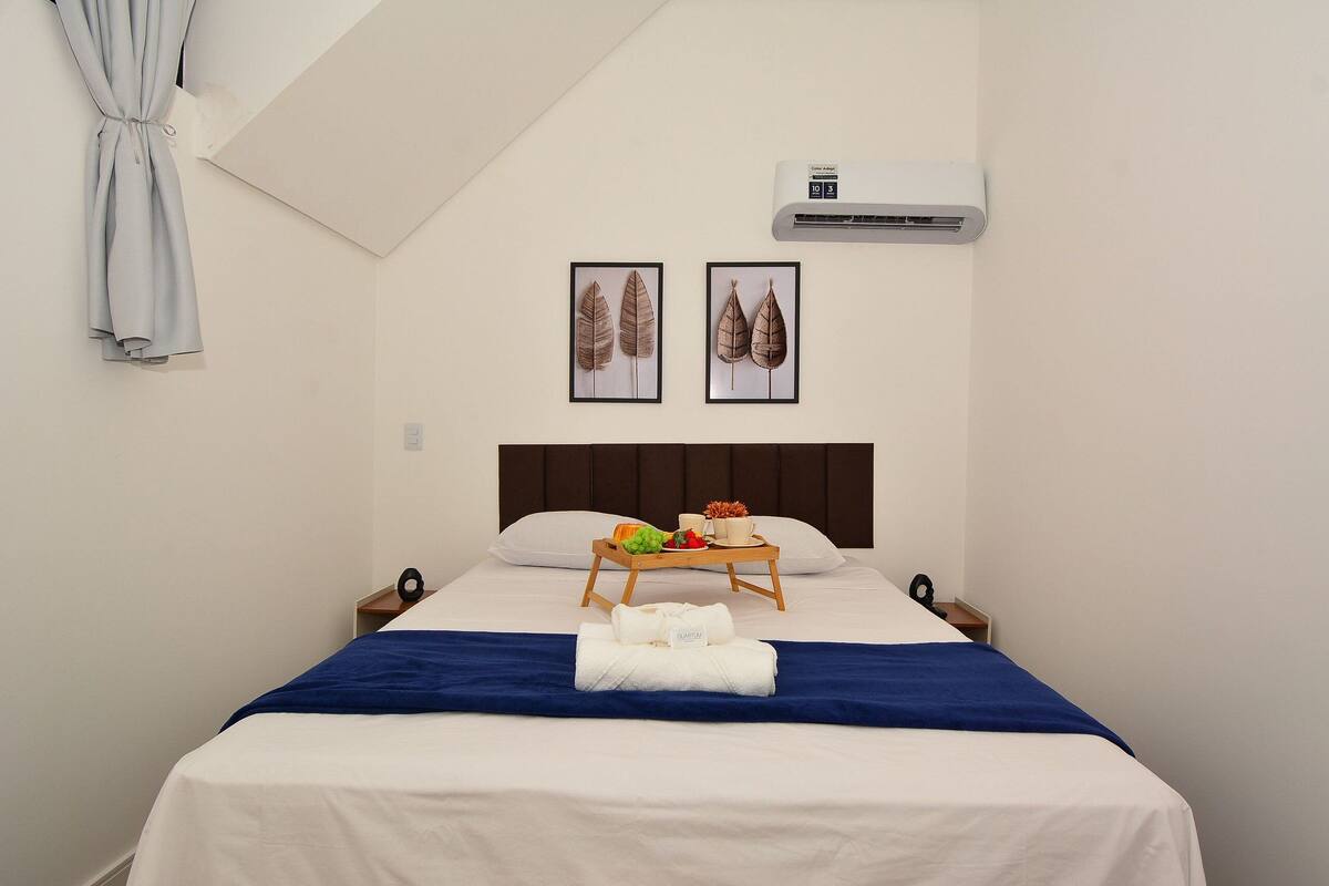 A neatly made bed with a blue blanket, a tray with fruits and a cup, and two framed leaf pictures on the wall.