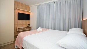 Hotelkamer met een bed, een flatscreen televisie aan de muur, een houten kast en een groot raam met gordijnen.