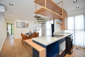 Una cocina moderna con una isla integrada, una zona de comedor con sillas y una escalera que sube a otro nivel.
