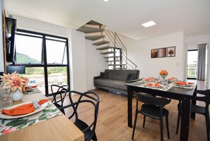 A modern living space with a dining area, a sofa, a staircase, and a view through large windows. - Residencial Germany (Florianópolis)