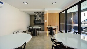 Een moderne eethoek met ronde tafels en zwarte stoelen, een keuken op de achtergrond en grote ramen met uitzicht.