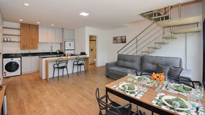 Een moderne keuken met een centraal eiland, een eethoek met een tafel gedekt voor vier personen, en een trap die leidt naar een hoger niveau.