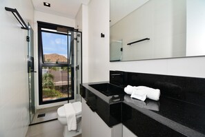 Un baño moderno con cabina de ducha de vidrio, encimera negra y inodoro blanco.