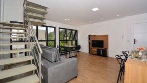 Um espaço de estar moderno com escada, sofá cinzento, área de jantar e televisão.