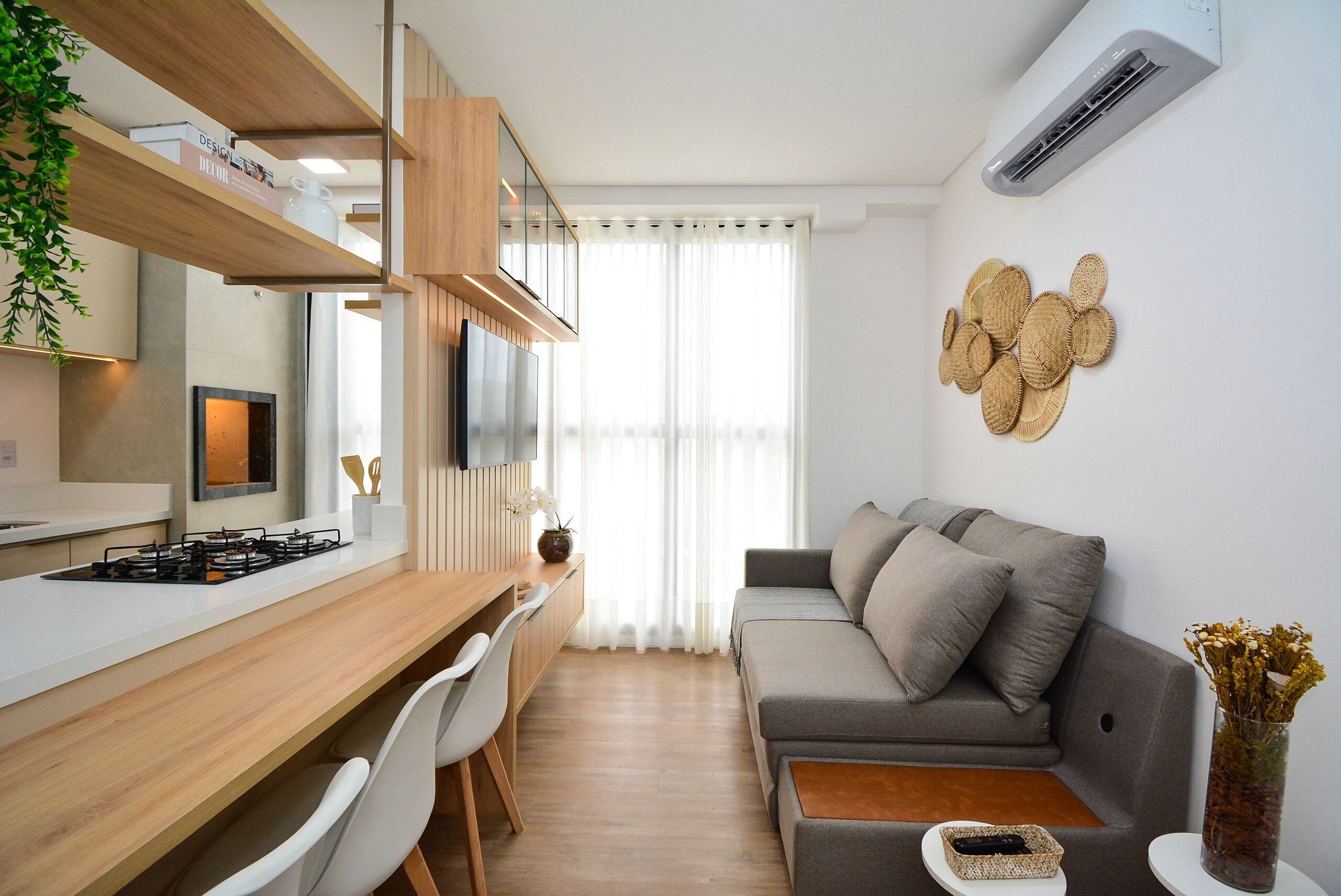A modern kitchen with a wooden countertop, white chairs, a grey sofa, and a wall-mounted air conditioner.