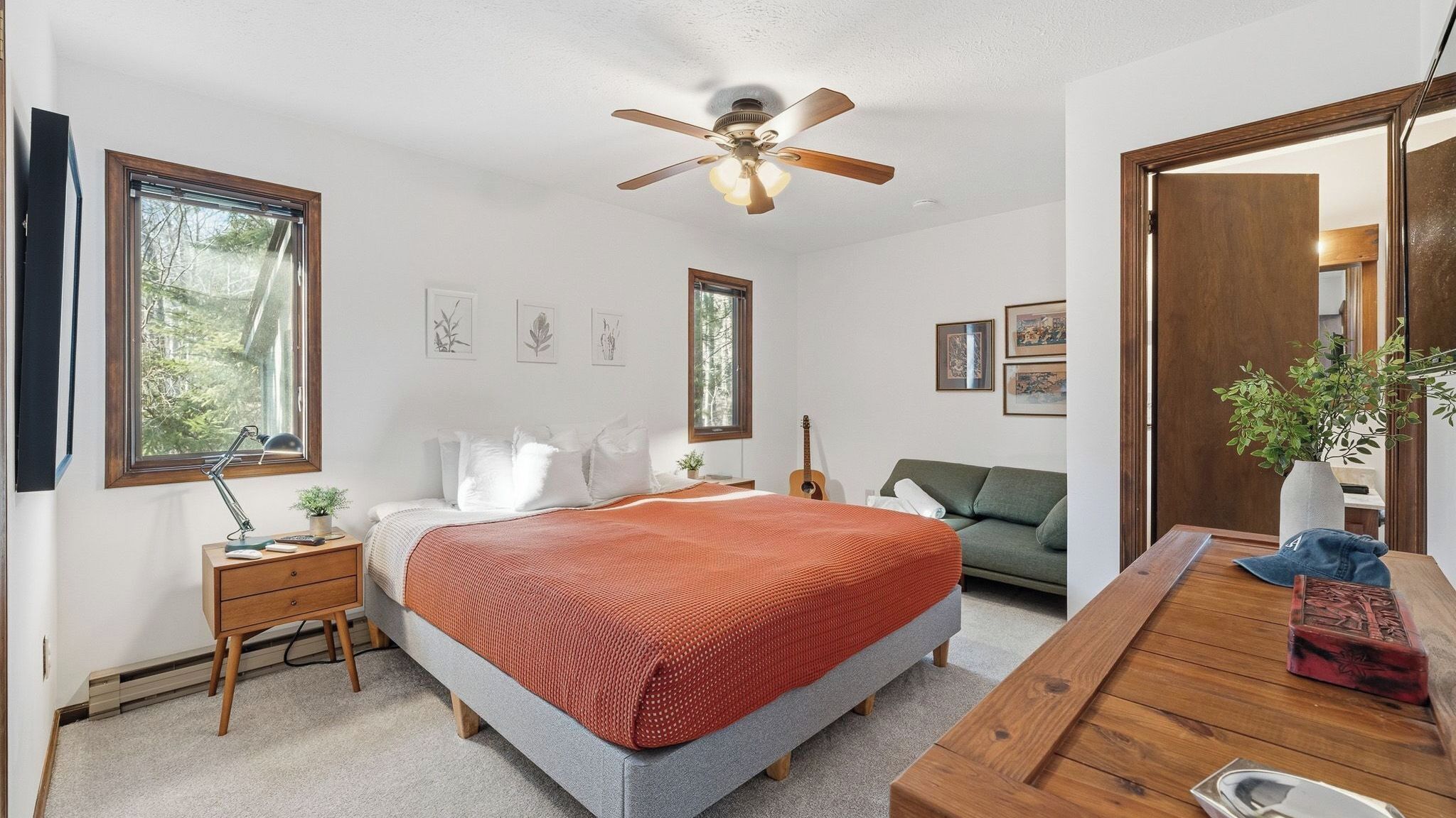 A bedroom with a bed, a desk, a guitar, a sofa, and a ceiling fan.