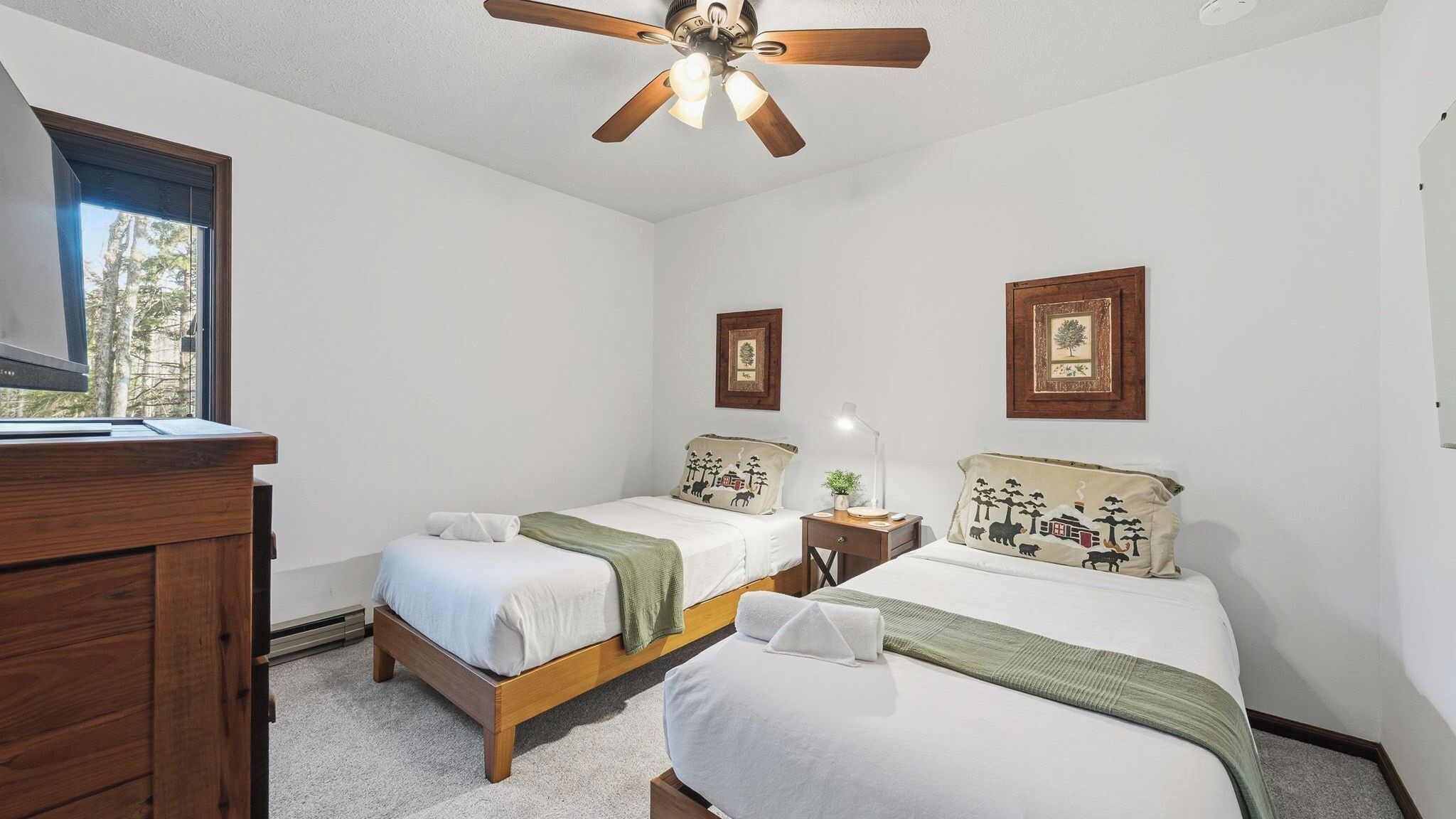 Ein Schlafzimmer mit zwei Betten, einer Holzkommode, einem Deckenventilator und gerahmten Bildern an der Wand.