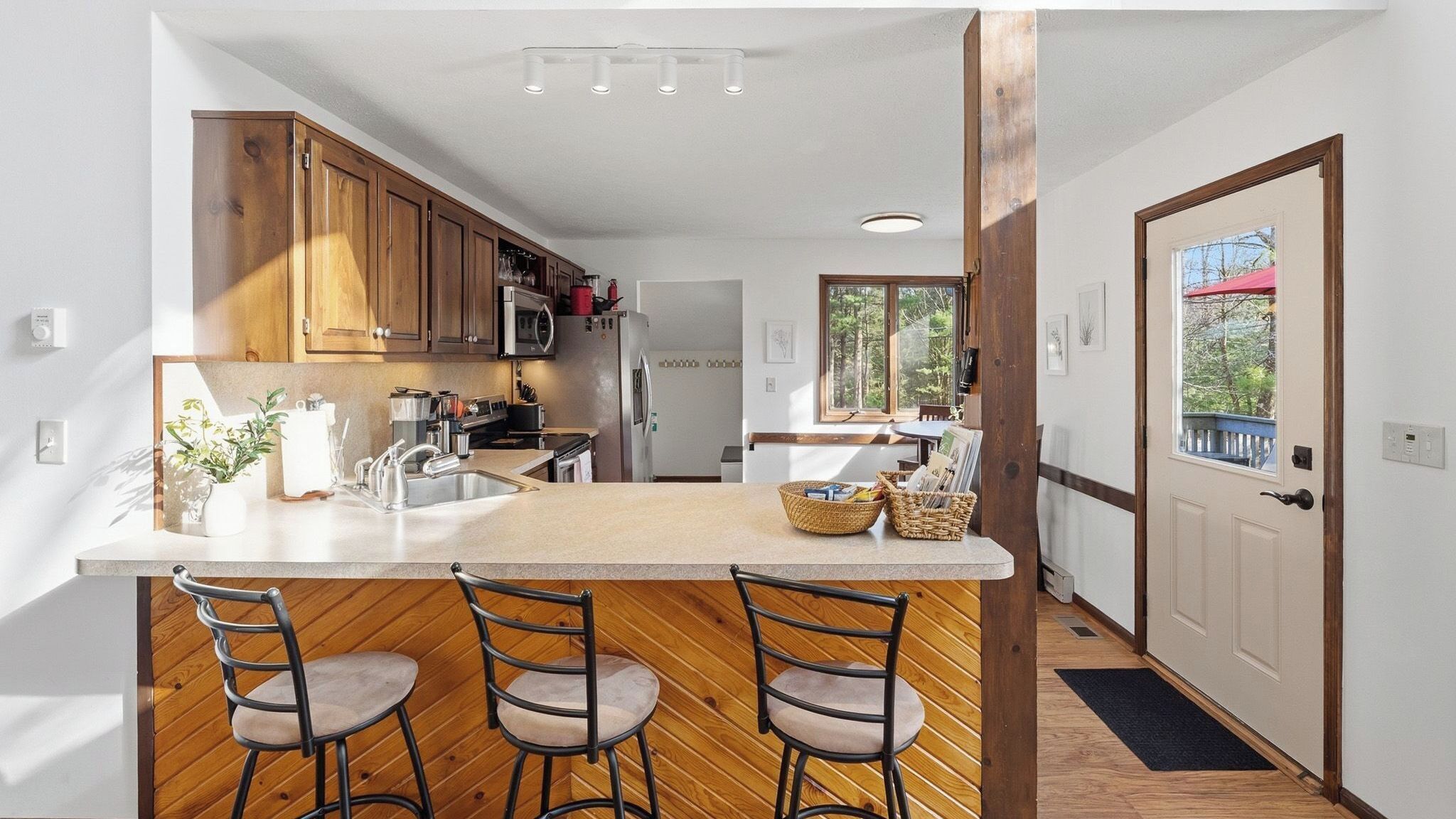 A kitchen with wooden cabinets, a central island with bar stools, and a view through a door to a balcony.