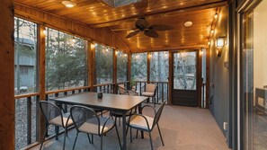 A wooden-paneled room with a table and chairs, large windows, and a ceiling fan. - Escape the City by Avantstay Screened Sunroom + Stone Fireplace + Cathedral Ceilings Lake Naomi Club + Pocono Pines (Pocono Pines)