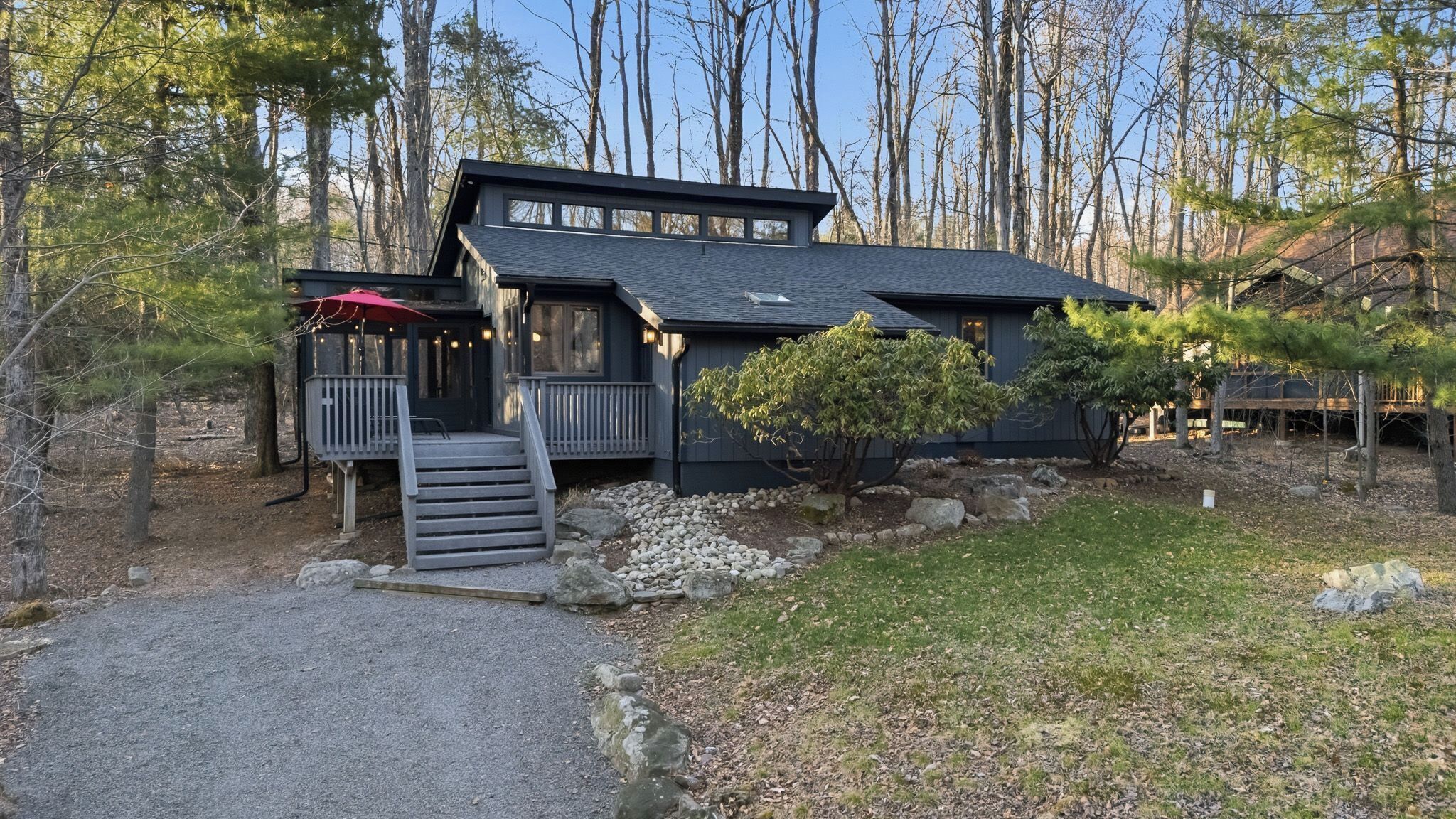 Une cabane avec une véranda, des marches et un petit arbre devant.