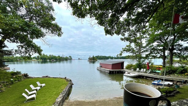 A lakeside view with a dock, lounge chairs, and a red building. - 1000 Islands Cottage Rental with sandy beach and amazing view.  Boat access only (Leeds And The Thousand Islands)