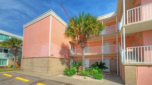 A multi-story building with balconies, a palm tree, and a brick base. - Gulf View Efficiency by Avantstay. Steps to Beach + Boardwalk 2 Pools + Pickleball Access Coastal Studio (Port Aransas)