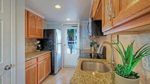 A kitchen with wooden cabinets, a stainless steel refrigerator, granite countertops, a sink, and a potted plant. - Gulf View Efficiency by Avantstay. Steps to Beach + Boardwalk 2 Pools + Pickleball Access Coastal Studio (Port Aransas)