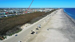 Vista aérea de una zona costera con playa, una carretera bordeada de vehículos y edificios al fondo.