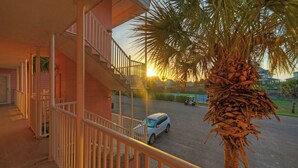 Un edificio residencial con una escalera, un coche aparcado y una palmera.