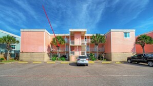 Un edificio de varios pisos con balcones, estacionamiento y palmeras.