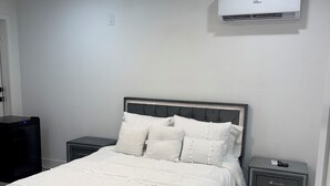 Ein Schlafzimmer mit einem Bett, zwei Nachttischen, einem Deckenventilator, einer Klimaanlage und einem an der Wand befestigten Fernseher.