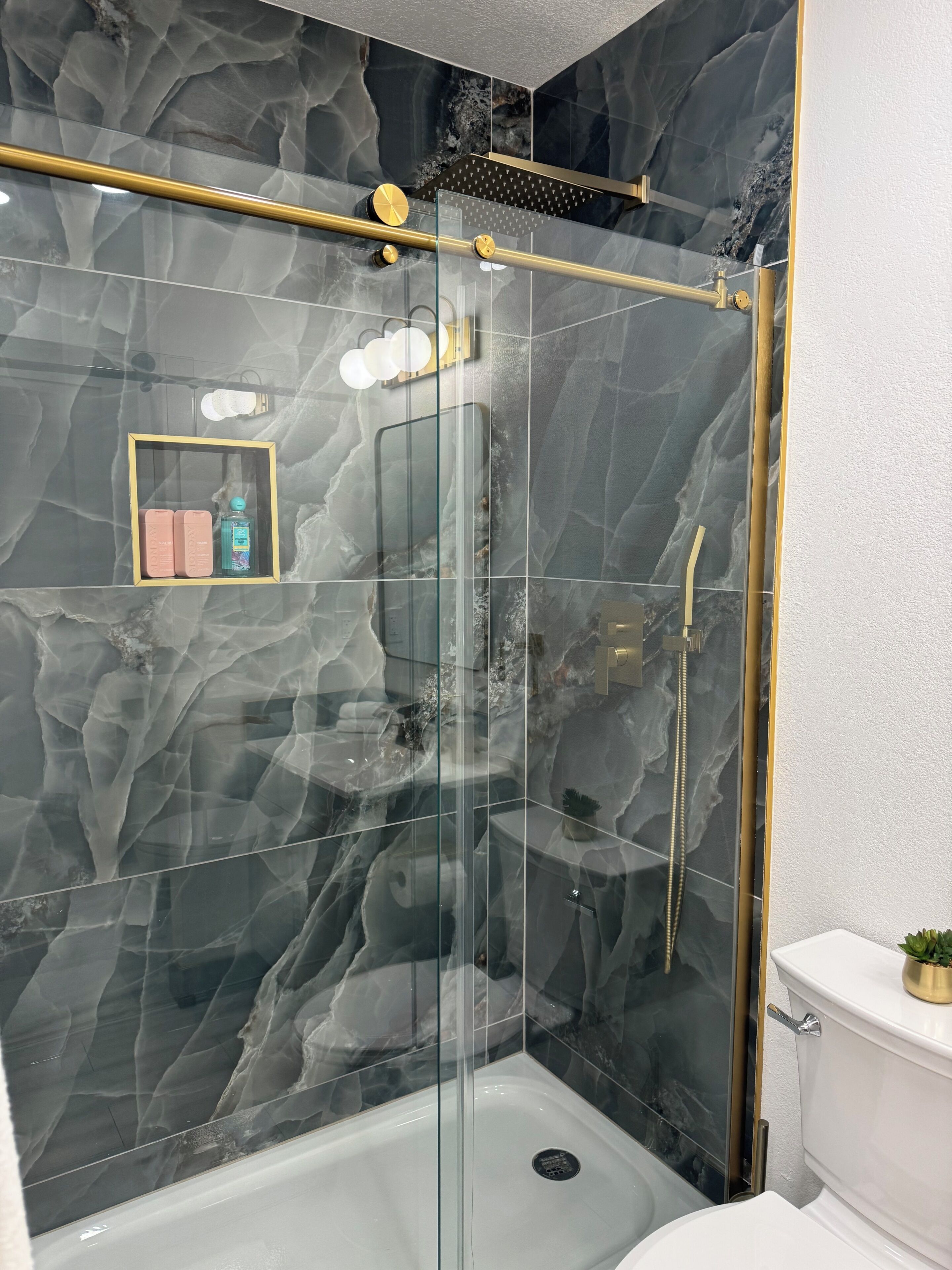 Une salle de bain moderne avec une douche à parois de verre, des murs en marbre et une pomme de douche encadrée d’or.