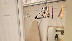Ein Zimmer mit Spiegel, Bügelbrett, Kleiderhaken und einer Pendelleuchte.