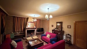 A living room with a fireplace, red and blue sofas, a television, and a wooden cabinet. - Montesión 71 Villa with swimming pool, Puy du Fou (Toledo)