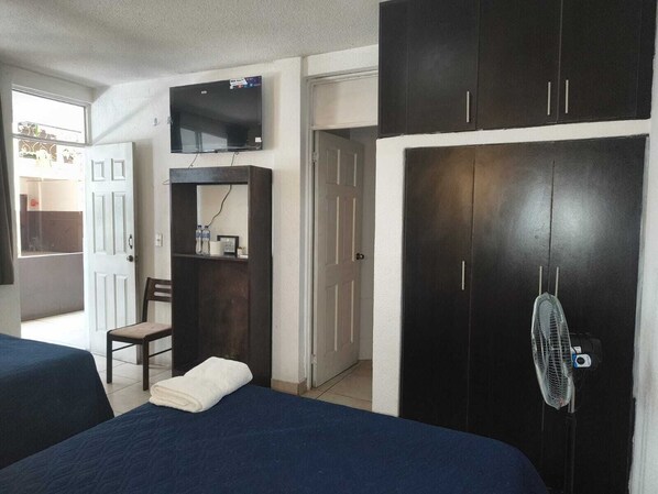 A bedroom with two beds, a TV, a wardrobe, a chair, and a fan. - Hotel Las Gardenias (Guatemala City)