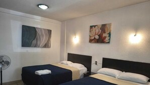 Hotellihuone, jossa on kaksi erillistä sänkyä, lattiatuuletin ja kaksi seinään kiinnitettyä valaisinta.