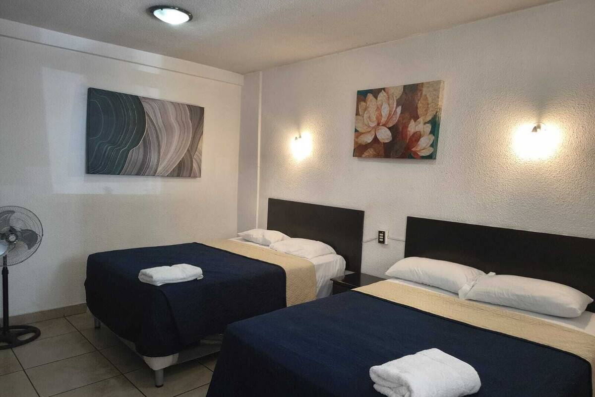 Ein Hotelzimmer mit zwei Einzelbetten, einem Standventilator und zwei Wandleuchten.