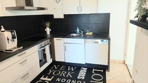 A modern kitchen with a black and white backsplash, stainless steel appliances, and a black and white rug with 'New York, Paris, London' text. - HC 104 big apartement with pool and garden (Haidershofen)