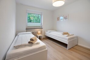 Ein Schlafzimmer mit zwei Betten, einem Fenster mit Jalousien, einem Nachttisch mit Lampe und einem Bild an der Wand.