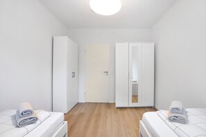 A room with two beds, a wardrobe, and a door leading to another room. - Apartment Allgäunest Wangen – Stylish Stay for Up to 5 Guests (Wangen im Allgäu)