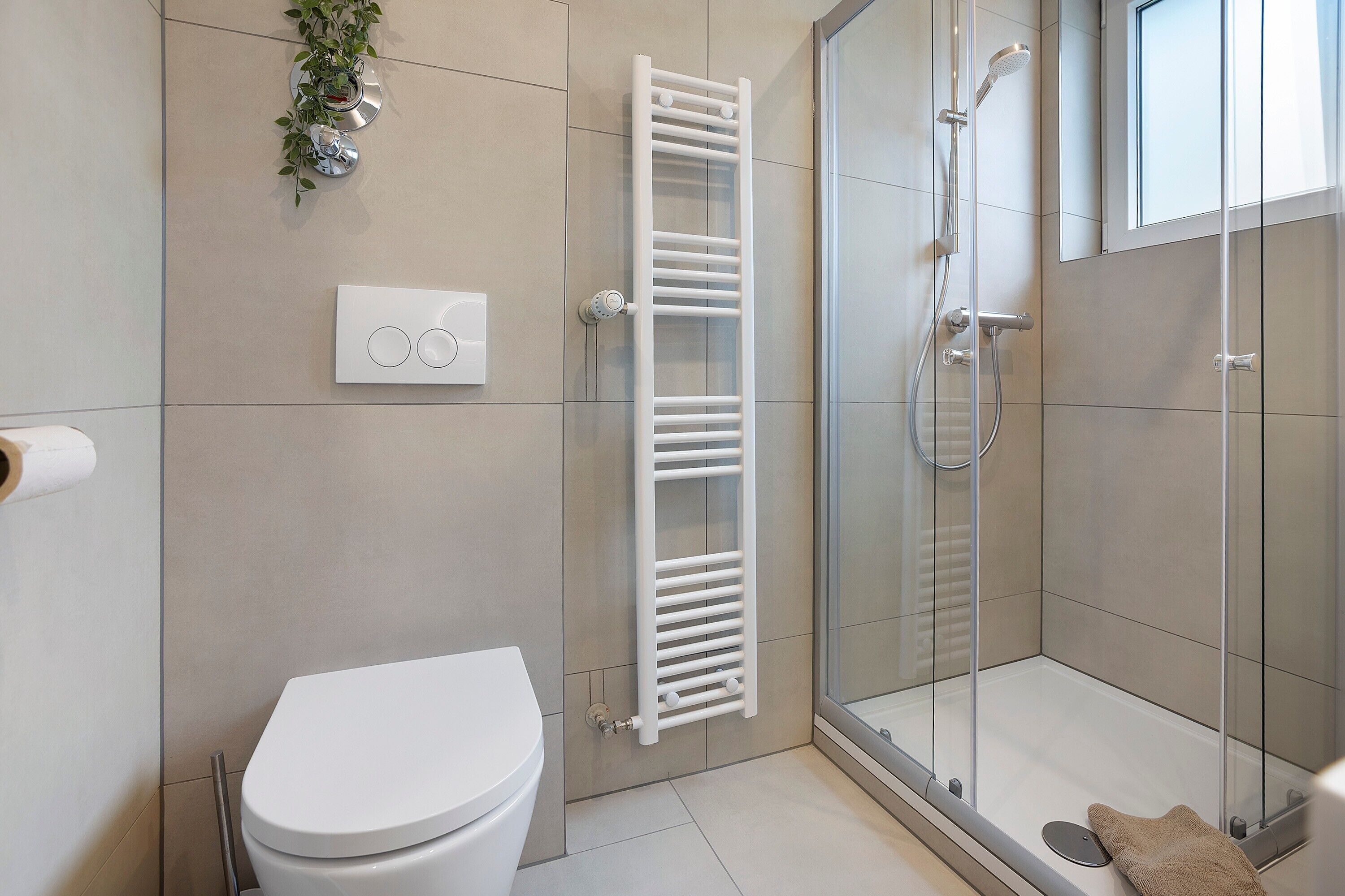 Ein modernes Badezimmer mit Toilette, einer gläsernen Dusche, einem weißen Handtuchhalter und einem Wandthermostat.