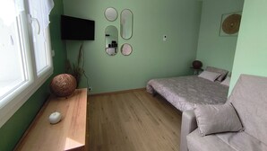 Una habitación con cama, sofá, escritorio de madera, televisor y espejo en la pared.