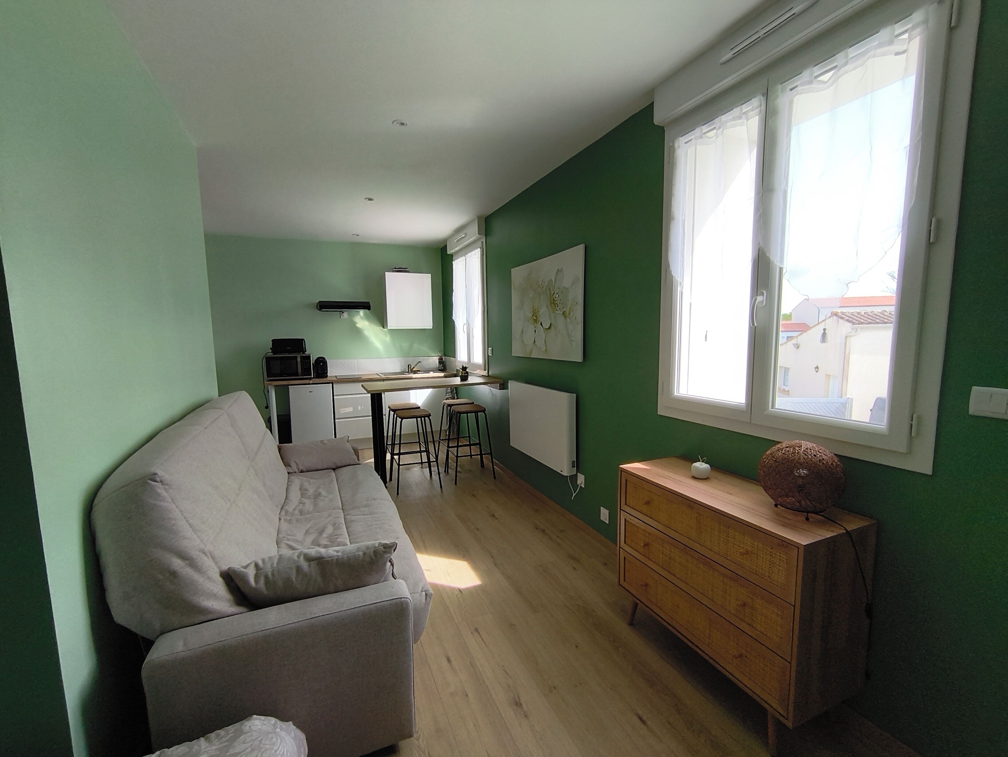A compact living space with a kitchenette, a sofa, a wooden dresser, and a window with a view.