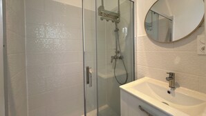 Un baño con cabina de ducha de vidrio, un lavamanos blanco y un espejo redondo.