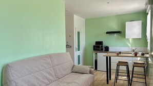 Un espacio habitable compacto con sofá, kitchenette y zona de comedor con taburetes.
