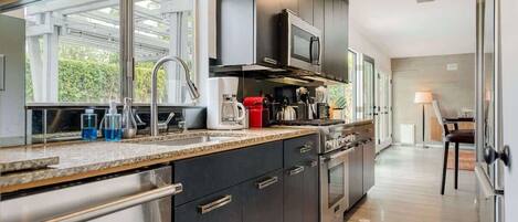 A modern kitchen with dark cabinets, stainless steel appliances, and a large window providing natural light.