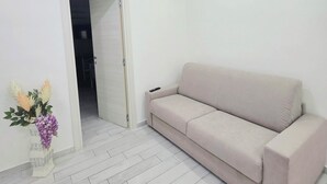 Una habitación con un sofá color beige, una puerta blanca y un florero con flores.
