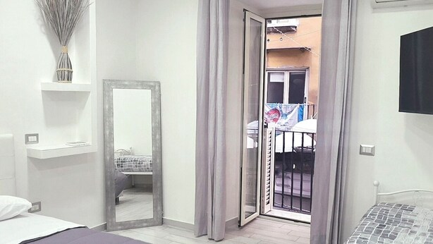 Un dormitorio con cama, mesita de noche, espejo y armario. Cuenta con un balcón con barandilla y vistas al exterior.