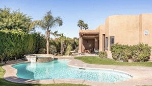 Ein Pool mit geschwungener Form, umgeben von einem gepflegten Rasen und Palmen.