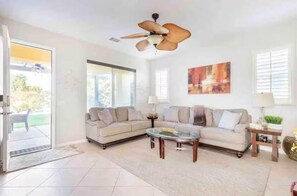 A living room with two sofas, a glass coffee table, a ceiling fan, and a large window.