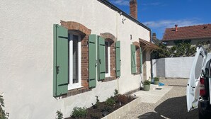 Et hus med grønne skodder, hvide vægge og en have med planter samt et espalier med træ.