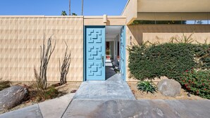 Un edificio moderno con fachada geométrica, una puerta azul y un sendero que lleva a la entrada.