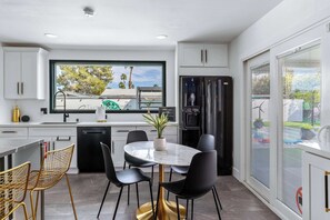 Eine moderne Küche mit weißen Schränken, einem schwarzen Kühlschrank, einem Esstisch mit Stühlen und einem großen Fenster.