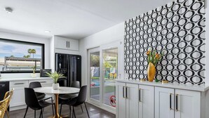 A modern kitchen with white cabinets, a dining area with black chairs, and a patterned wall. - 4BR Resort Home w Pool, Hot Tub & Fire Pit (Palm Springs)