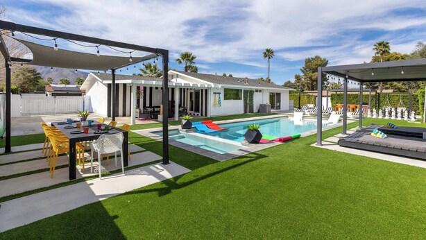 A backyard with a swimming pool, a covered patio, and a lawn. - 4BR Resort Home w Pool, Hot Tub & Fire Pit (Palm Springs)