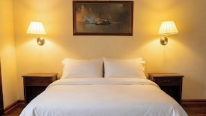 Una cama bien hecha con sábanas blancas, dos mesitas de noche con lámparas y un cuadro en la pared.