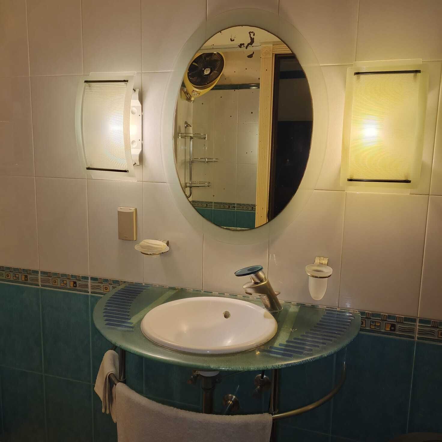 Une salle de bain avec un miroir rond, un lavabo avec un récipient en verre et une serviette accrochée au mur.