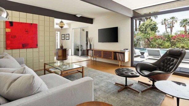 Ein modernes Wohnzimmer mit einer Couch, einem Glastisch, einem Ledersessel und einem an der Wand befestigten Fernseher.