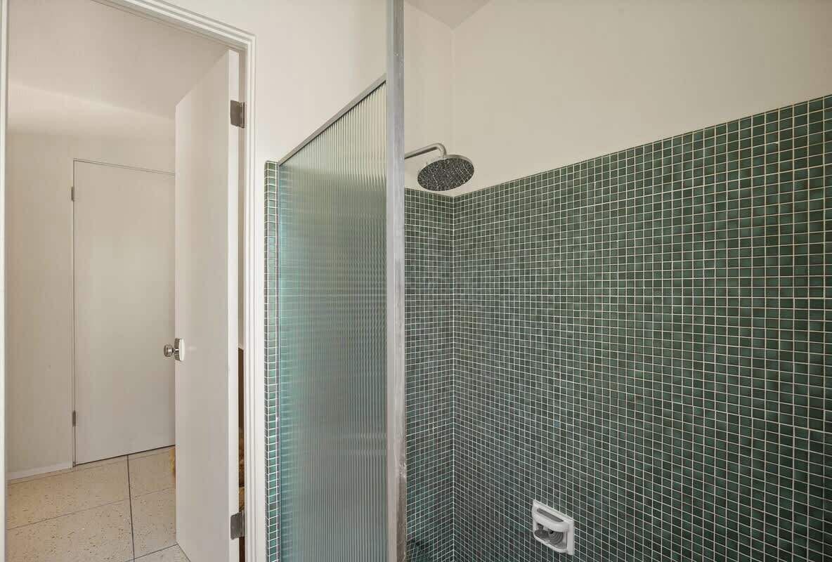 Een badkamer met een douche, betegelde wanden en een deur.