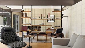 Ein modernes Wohnzimmer mit einem schwarzen Ledersessel, einem grauen Sofa, einem Holztisch und einem Bücherregal mit Büchern und Dekoration.